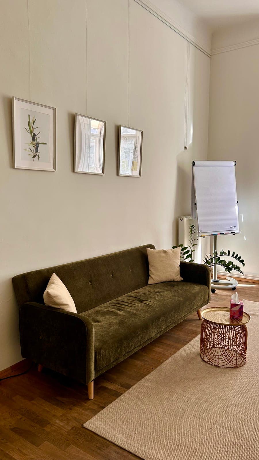 A green velvet sofa under three framed prints, with a flipchart in the corner